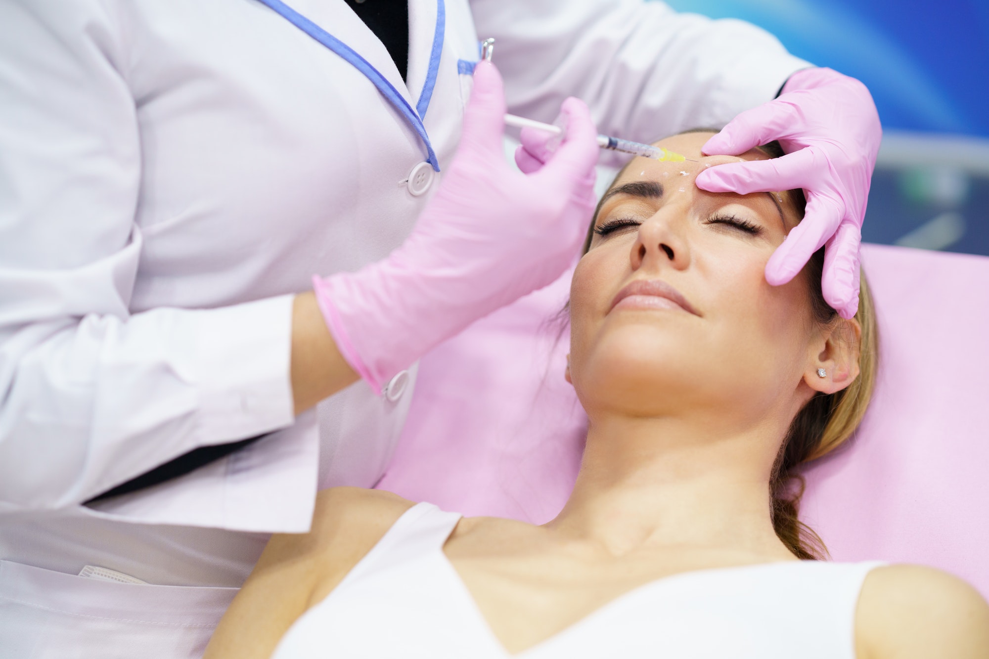 Aesthetic doctor injecting botulinum toxin into the forehead of her middle-aged patient